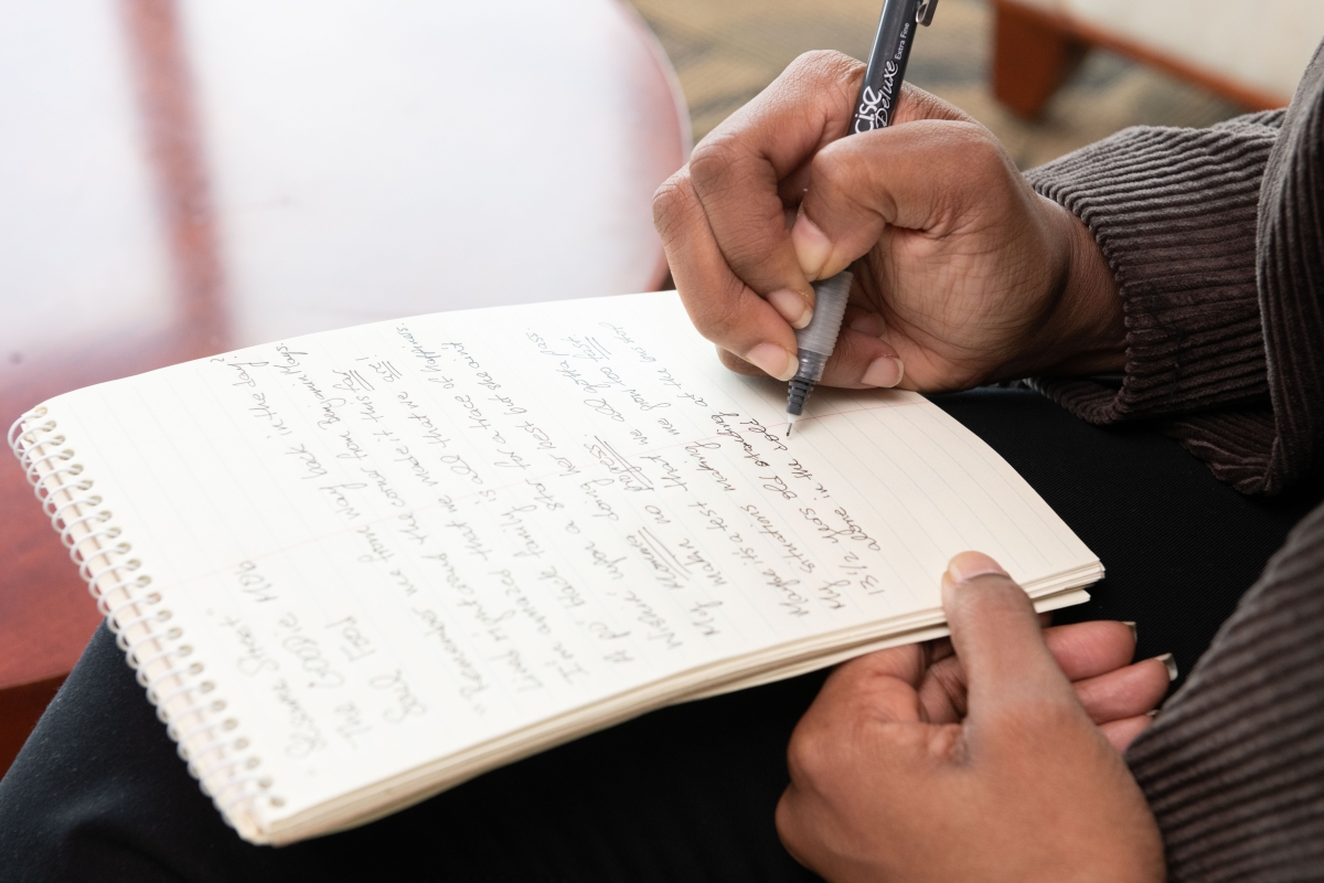 A photo of hands writing on a notepad