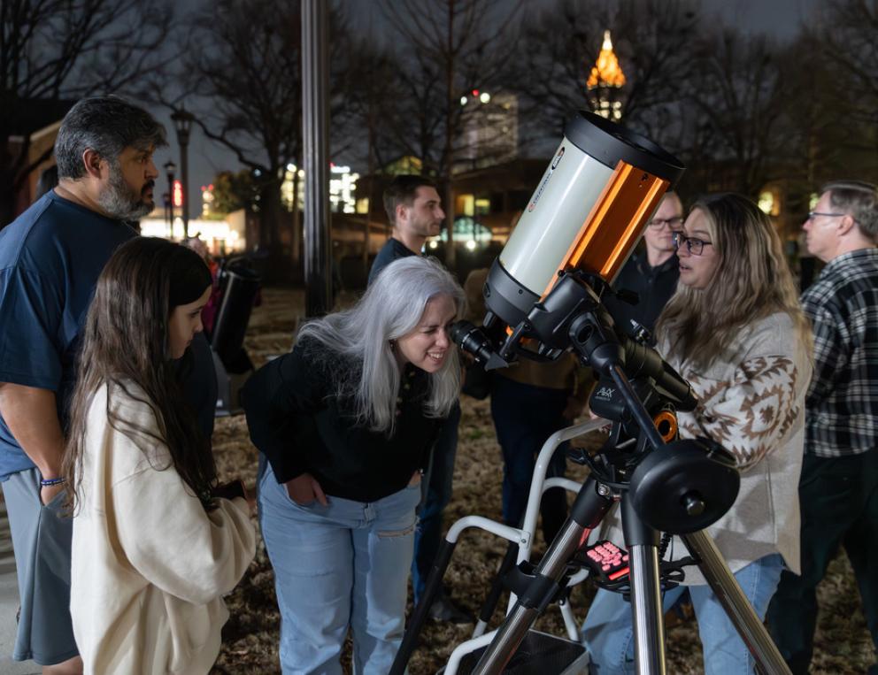 A professor and students looking through a telescope.