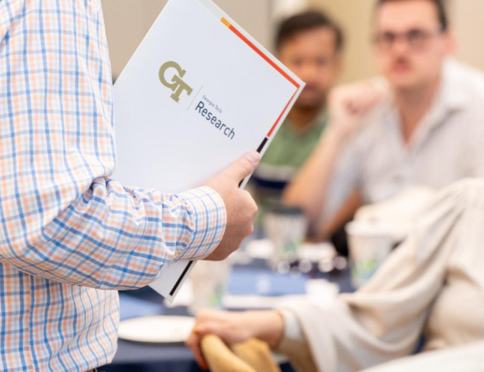 A person at faculty orientation holding a folder that reads, "GT Research."